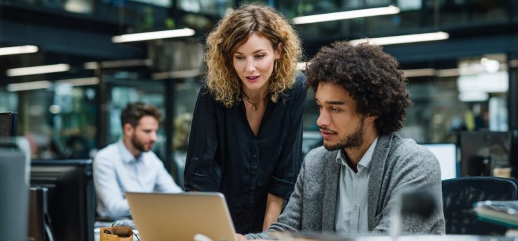 Três pessoas em um espaço de trabalho, incluindo um gerente conversando com um funcionário em sua mesa, ilustram o modelo líder-líder.