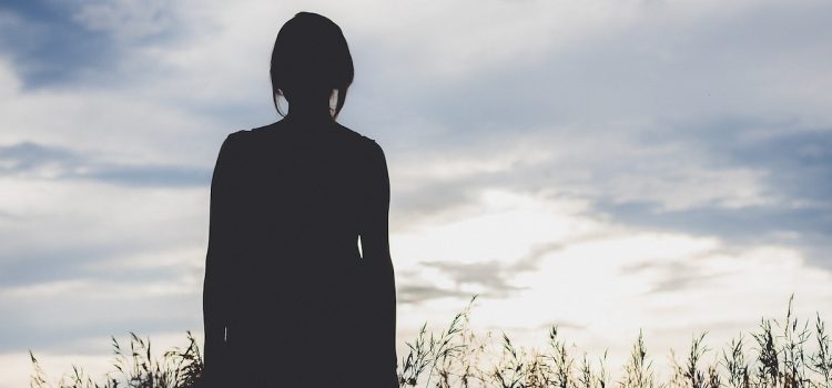 A silhouette of a woman looking at the sky in a field.