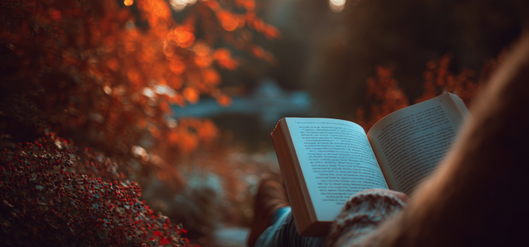 A woman reading a book outside in autumn with trees in the background