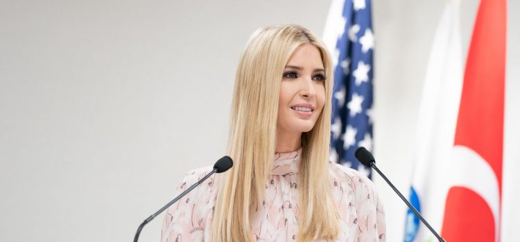 Ivanka Trump talking into microphones in front of two flags.