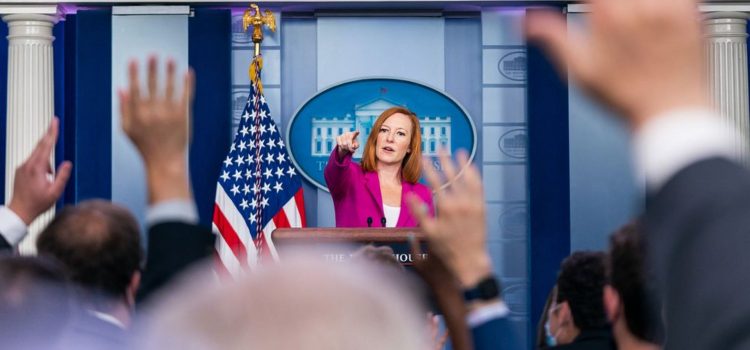 Jen Psaki pointing at journalists raising hands in the White House briefing room.