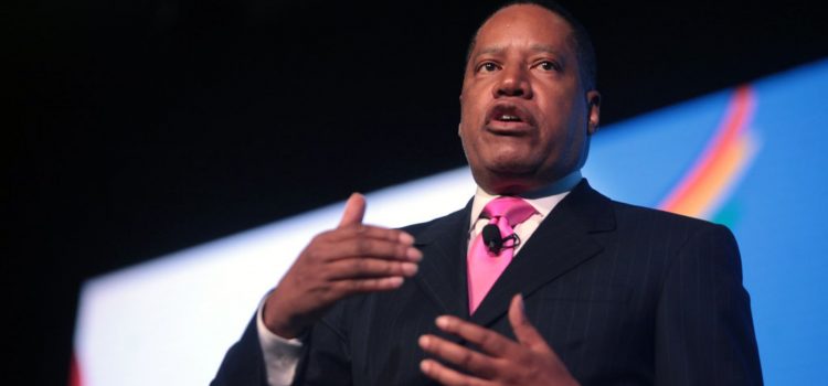 Larry Elder, conservative media figure, speaking on stage dressed in a suit