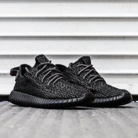 A pair of black Yeezy Adidas shoes against a white wall.
