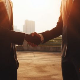 Two men in suits shaking hands outside, showing how to hire the right person.