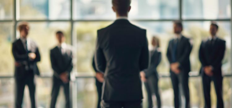 A functional manager standing in front of a team of employees near a glass window.