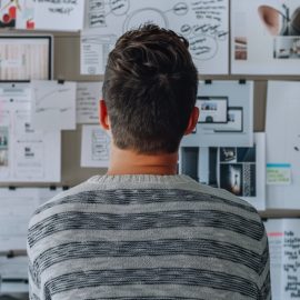 A man looking at a wall of papers and notes using outcome-based planning.