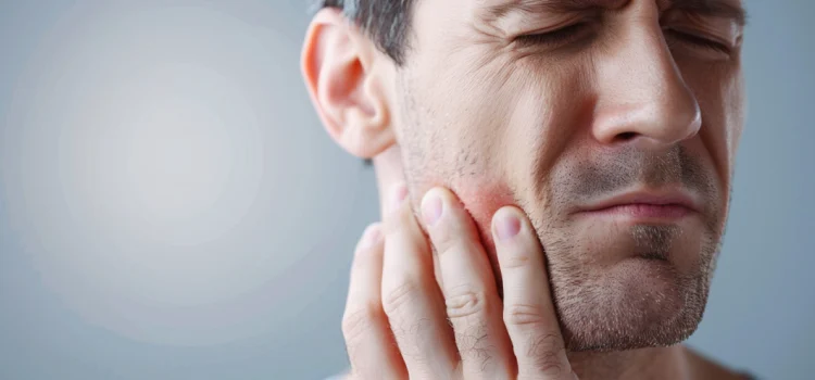 How Jaw Problems Can Lead to Other Health Issues A man with jaw problems who is touching his jaw with a look of pain on his face
