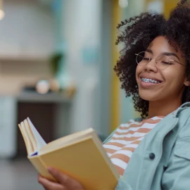 A woman with braces reading a book while sitting on a dentist chair in a dental office