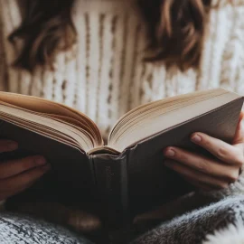 A woman reading a book wearing a white sweater