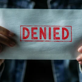 Hands holding an envelope that has the word "denied" stamped on it with red ink because of the health insurance crisis in the US