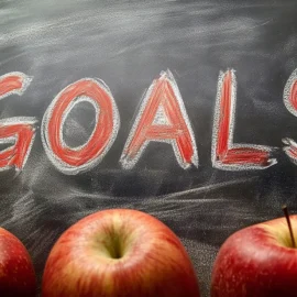 The word "GOALS" on a chalkboard with three apples, representing how to set realistic goals