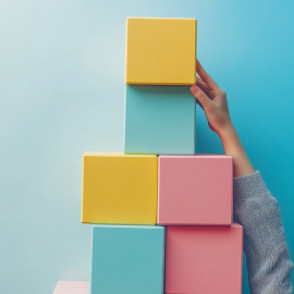A hand holding up a structure of colored blocks on a plain background