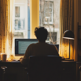A remote worker sitting at a desk in his home office in front of a window