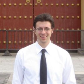 Journalist Ezra Klein standing in front of a door wearing a formal shirt and tie
