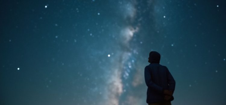 What Is Real? Adam Becker on Quantum Physics (Book Overview) Eine Person, die als Silhouette von hinten gesehen wird und zu den Sternen und der Milchstraße am Nachthimmel aufschaut