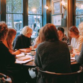 Ten women in a book club discussion sitting around a table in a restaurant