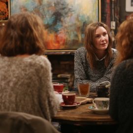Several woman in a book club discussion sitting around a table in a cafe with bookshelves
