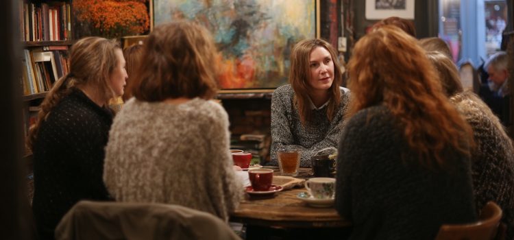 Several woman in a book club discussion sitting around a table in a cafe with bookshelves