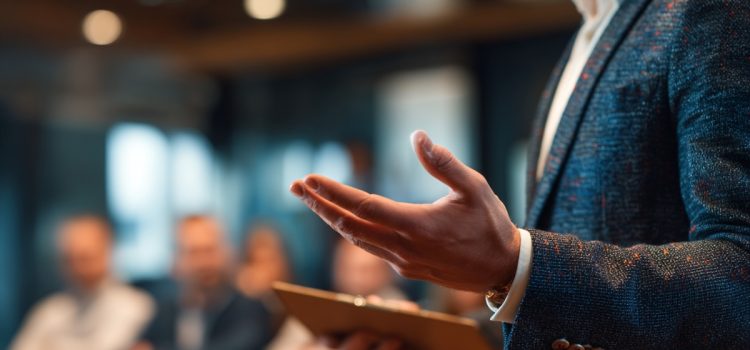 A man holding a tablet and conducting a sales pitch to a room full of potential clients