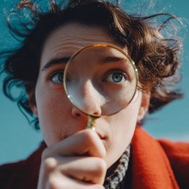 A close-up of a curious person with curly brown hair looking through a magnifying glass