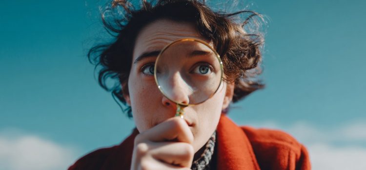 A close-up of a curious person with curly brown hair looking through a magnifying glass