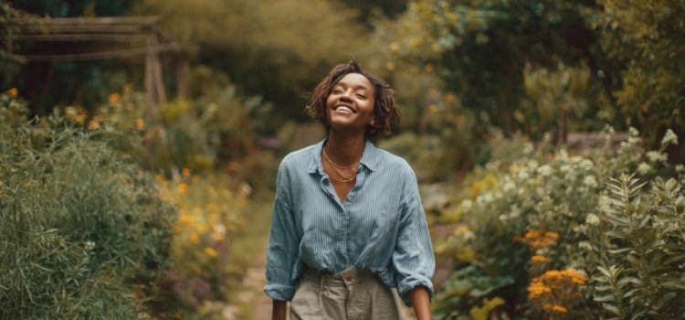 A young woman smiling and facing upward with her eyes closed walking through a flower garden