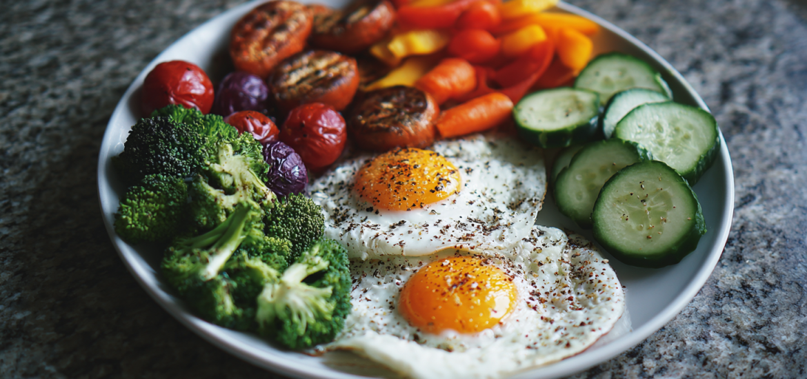 A plate of healthy food including broccoli, eggs, tomatoes, cucumber, carrots, and peppers for dieting