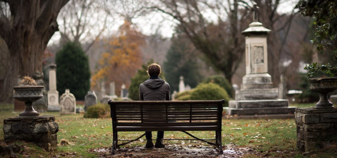 A man sitting and thinking on a bench in a cemetery, seen from behind, illustrates stoicism and death