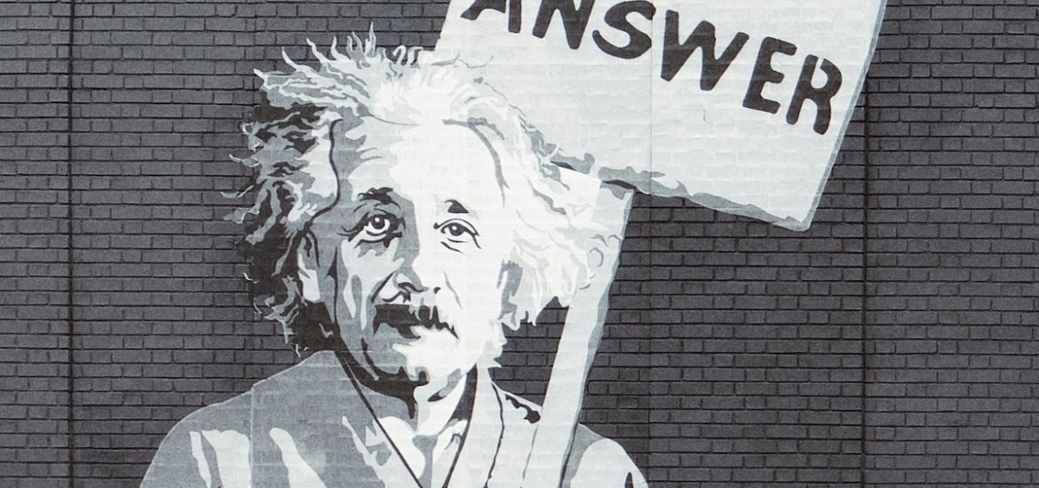 An artistic depiction of Albert Einstein on a brick wall, carrying a sign that says "Answer"