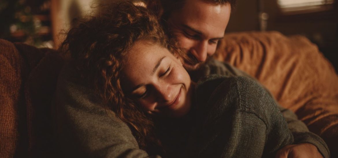 A man and a woman smiling and hugging on a couch because they are emotionally secure