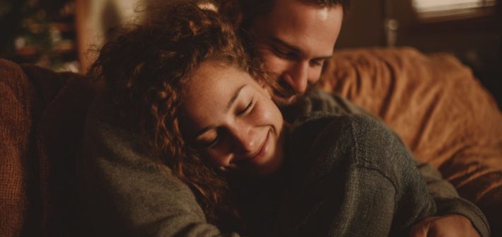 A man and a woman smiling and hugging on a couch because they are emotionally secure