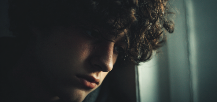 A socially isolated depressed young man leaning his head against a wall