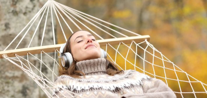 A woman relaxing in a hammock outside while wearing headphones