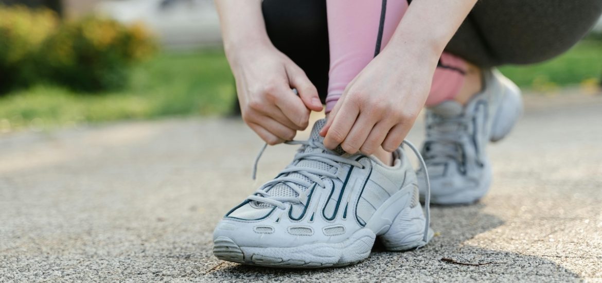 A close-up of a woman's hands lacing up running shoes illustrates how to motivate yourself to exercise