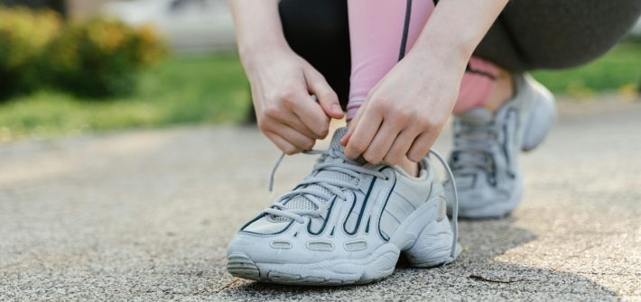 A close-up of a woman's hands lacing up running shoes illustrates how to motivate yourself to exercise
