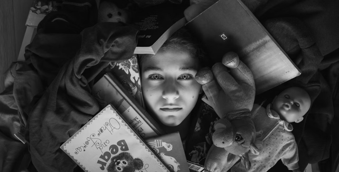 A black and white photo of a girl laying in a pile of clutter