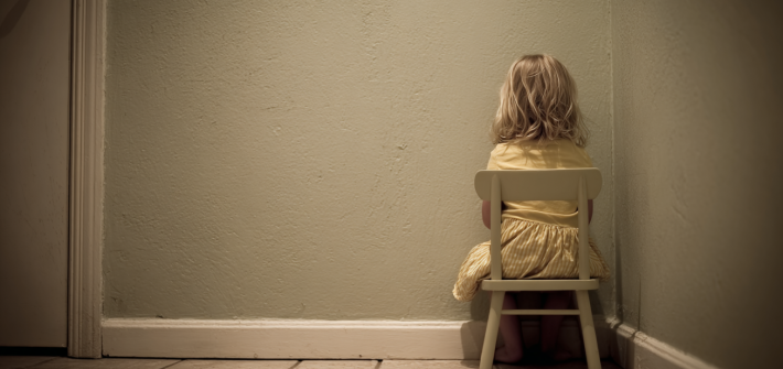 A young girl sitting in time out on a chair in a corner, representing traditional parenting methods