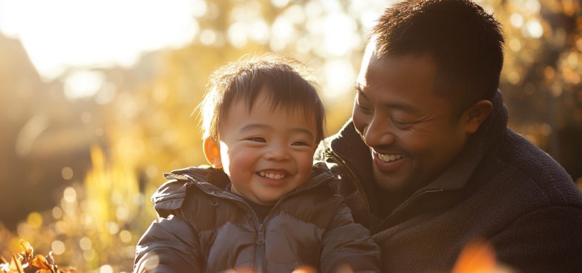 Smiling father and toddler son wearing jackets while outside among trees in the sunshine illustrate mindful parenting