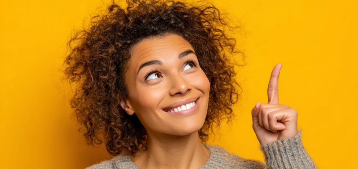 A smiling woman with curly hair looking and pointing upward illustrates how to stop feeling sorry for yourself