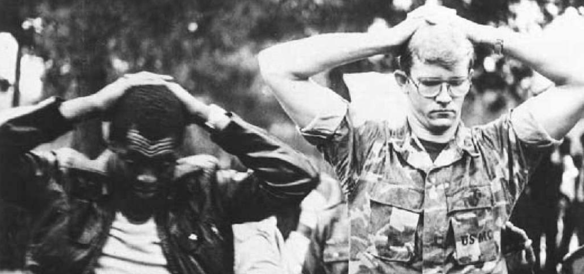 Two male American hostages (one in a USMC uniform) with their hands on their head during the Iran hostage crisis